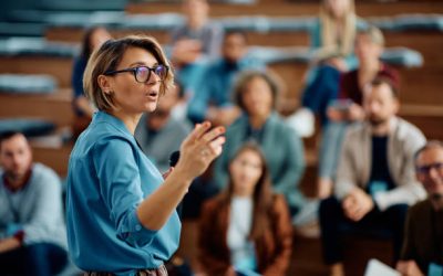 istockphoto-1783743772-612×612 Mid adult businesswoman talking to group of seminar attendees in conference hall.